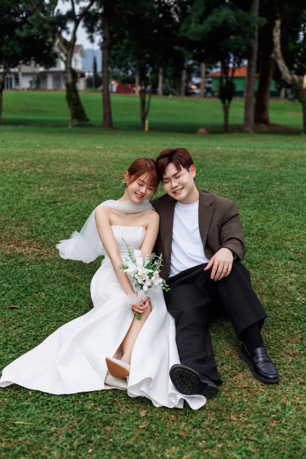 Clifford and Shuzhen seated together on the grass in wedding attire